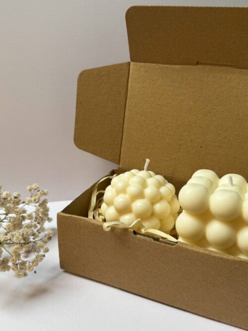 Świece sojowe w kształcie bubble dużej i kuli, zapakowane w pudełko prezentowe, w tle gipsówka